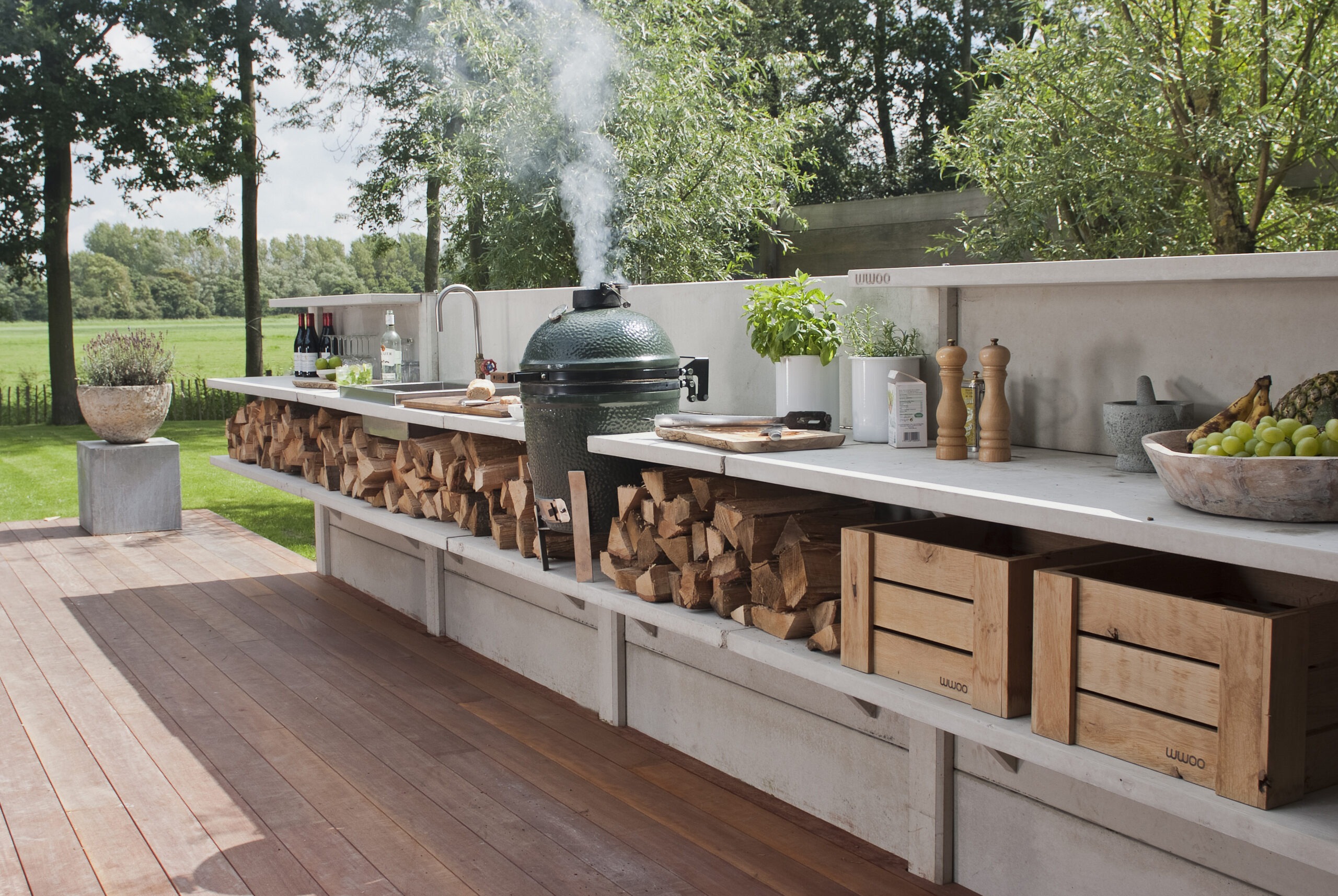 Fully stocked grey concrete kitchen with steaming green egg, sink on a wooden terrace in green garden